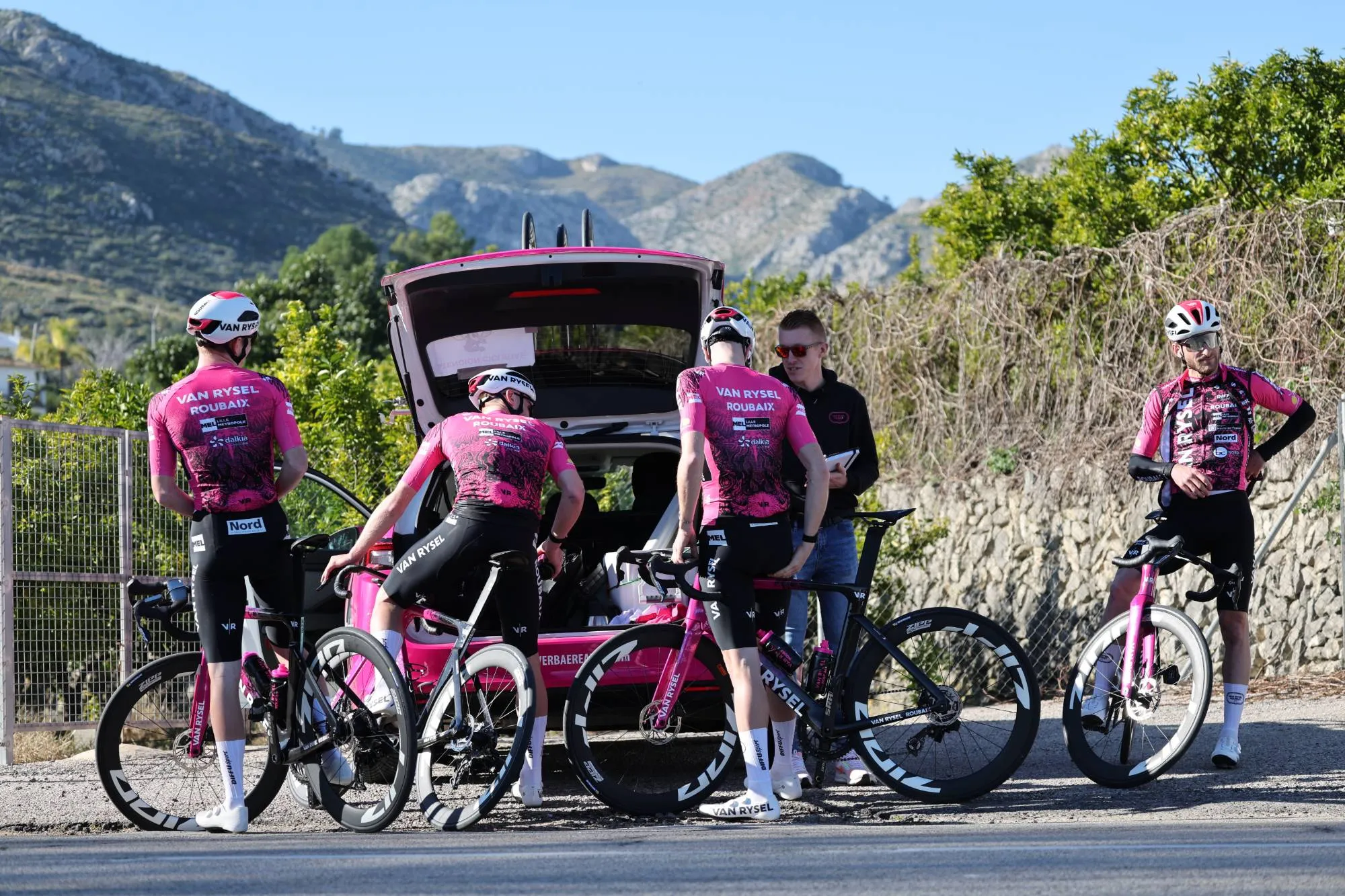 Maxim Frémeaux, tablette en main, avec les coureurs de la Team Van Rysel Roubaix autour de la voiture d’équipe en stage